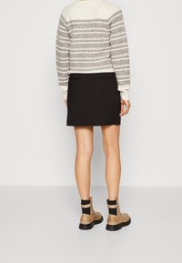 Maglione lavorato a maglia con un design a motivo crema e grigio, abbinato a una mini gonna nera e stivaletti alla caviglia color nocciola con dettagli elastici neri.
