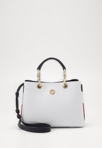 Hvid struktureret læderhåndtaske med guldfarvede detaljer, dobbelte hænder og en justerbar skulderrem. Udstyret med røde og sorte accenter.