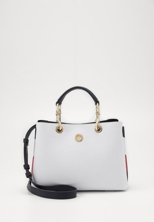 Sac à main en cuir blanc texturé avec quincaillerie dorée, deux poignées et une bandoulière réglable. Présente des accents rouges et noirs.