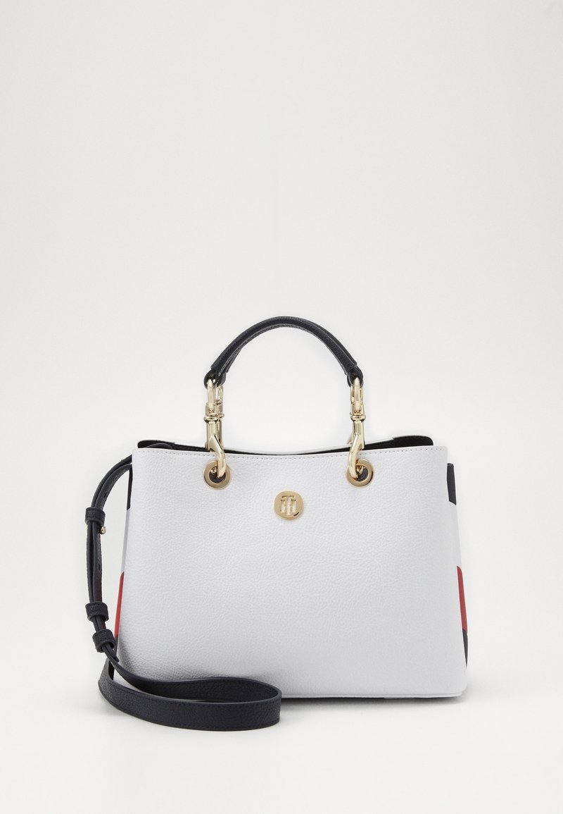 Hvid struktureret læderhåndtaske med guldfarvede detaljer, dobbelte hænder og en justerbar skulderrem. Udstyret med røde og sorte accenter.