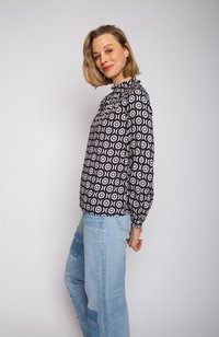 Langärmlige Bluse mit rundem Halsausschnitt und schwarz-weißer Kreisstruktur. Kombiniert mit hellblauen, beschädigten Jeans.