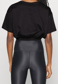 Černé zkrácené tričko s volným střihem, elastickým lemem a krátkými rukávy, v kombinaci s černými legínami s vysokým pasem, hladkou texturou a elastickým materiálem.