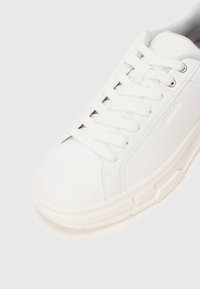 Sneaker bassa bianca con lacci bianchi, fodera interna grigia, suola testurizzata e nome del brand inciso in modo sottile di lato.