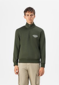 Grøn zip-up sweatshirt med høj krave og ribbede manchetter. Har et hvidt logo på brystet. Blød, glat tekstur og tætsiddende design.