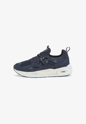 Zapatilla moderna azul marino con parte superior de malla y ante, suela blanca gruesa, forro interior negro y tira para tirar en el talón, vista lateral.