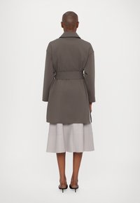 Grau belted Mantel mit breitem Kragen, im A-Linien-Silhouette. Getragen über einem hellgrauen, plissierten Rock. Glatte Textur.