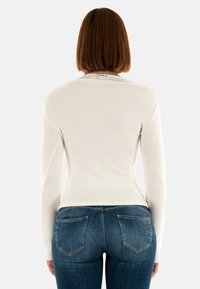Maglietta bianca a maniche lunghe con una vestibilità aderente, abbinata a jeans blu scuro con tasche posteriori e dettagli di cucitura chiara.