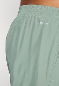 Heledad rohelised lühikesed püksid elastse vöökohtaga, millel on valge "AEROREADY" logo. Sile tekstuur ja hingav materjal.