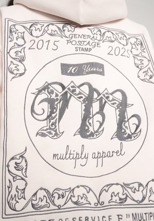 Felpa rosa chiaro con stampa grafica che ricorda un francobollo. Presenta lettere grigie intricate, accenti floreali e un banner "10 Anni".