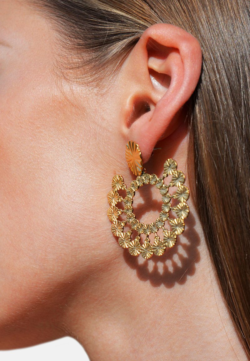 Boucles d'oreilles dorées présentant un design floral détaillé avec des accents circulaires, mettant en valeur des motifs complexes et une structure superposée.