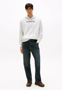 Haut à capuche gris clair avec le logo "Tommy Jeans", accompagné d'un jean droit bleu foncé et d'une ceinture noire. Les chaussures sont sombres avec des accents rouges.