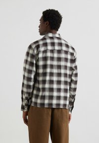 Bruine en crèmekleurige geruite flanellen shirt met een kraag, lange mouwen en knoopmanchetten. Bevat een rugpand en heeft een relaxte pasvorm.