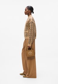 Un pull en laine beige avec un motif en relief, un pantalon beige surdimensionné et un petit sac à main marron portant un texte blanc ; des chaussures à imprimé léopard.