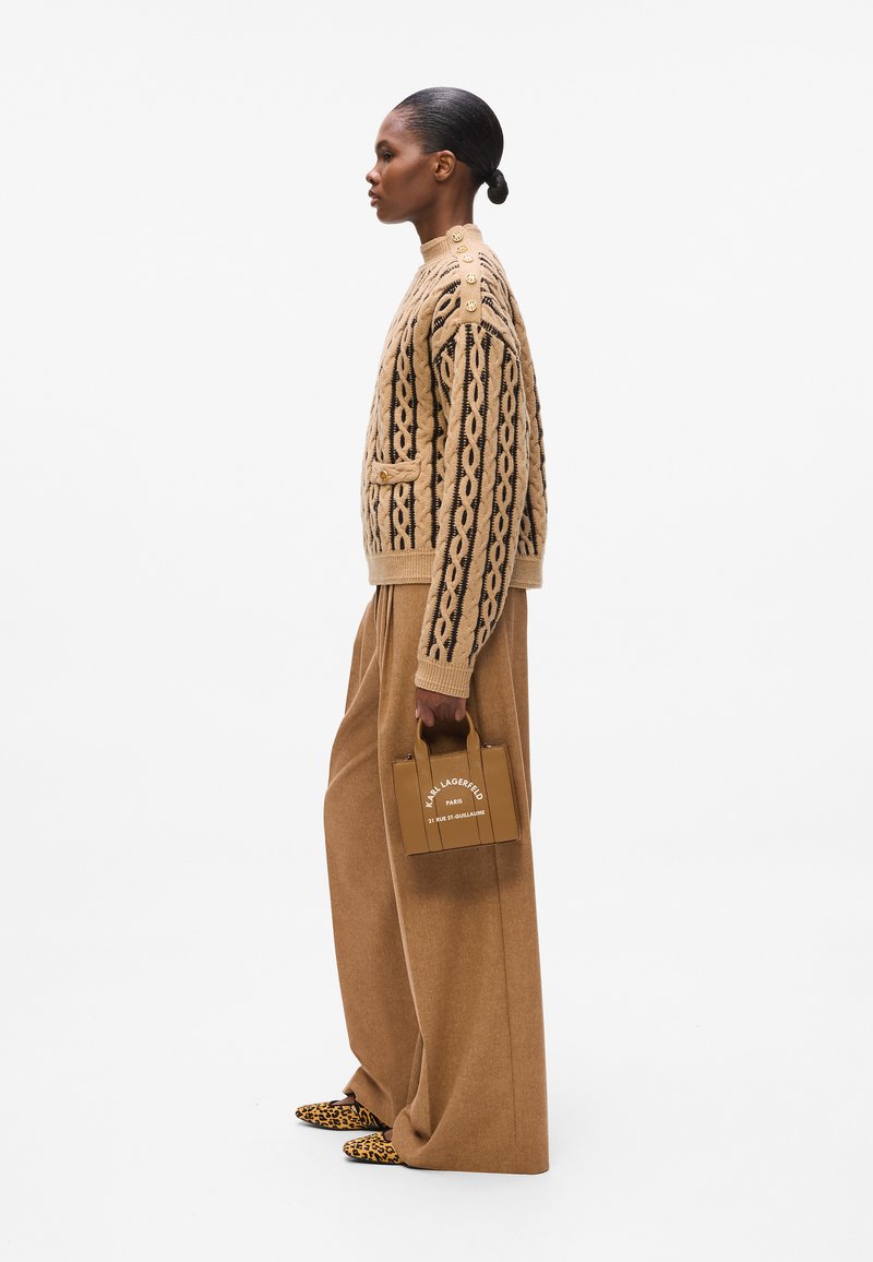 Un pull en laine beige avec un motif en relief, un pantalon beige surdimensionné et un petit sac à main marron portant un texte blanc ; des chaussures à imprimé léopard.