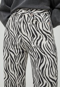 Pantalon en denim noir et blanc à motif zébré, avec poches avant et fermeture par bouton à la taille.