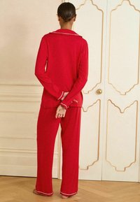 Rød pyjamas sæt i blødt stof med lange ærmer og lige bukser. Har hvid kant på kraven og manchetterne, med et enkelt design.