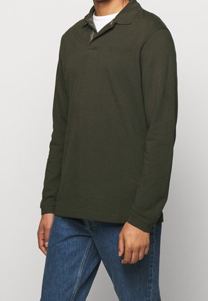 Koszula polo z długim rękawem w ciemnozielonym kolorze z bawełny, wyposażona w klasyczny kołnierzyk i kratkowe akcenty przy dekolcie, zestawiona z niebieskimi dżinsami.