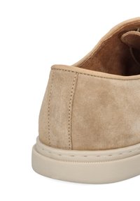 Beżowy zamszowy but z zaokrąglonym obcasem, miękką teksturą i kremową gumową podeszwą. Szczegół szwu wzdłuż obcasa dodaje subtelnej definicji.