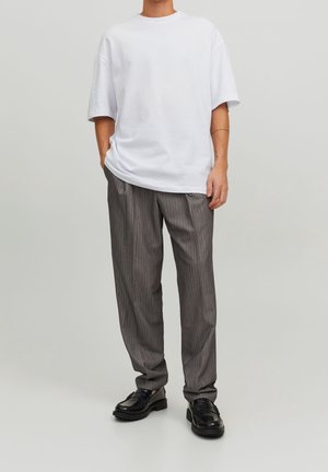 Weißes übergroßes T-Shirt mit rundem Ausschnitt, kombiniert mit grauen gestreiften Hosen und schwarzen Schnürschuhen. Flache Stoffstruktur, lockere Passform.