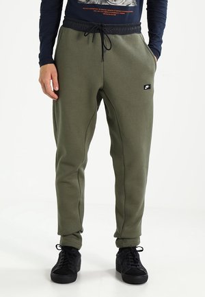 Olijfgroene sweatpants met elastische tailleband en trekkoord, voorzien van zijzakken en een kleine zwarte logopatch. G gedragen met zwarte sneakers.