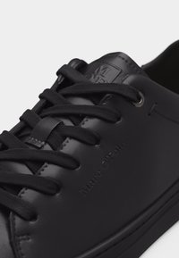 Baskets en cuir noir avec lacets noirs, logo "Marc O'Polo" embossé sur le côté et étiquette cousue sur la languette.