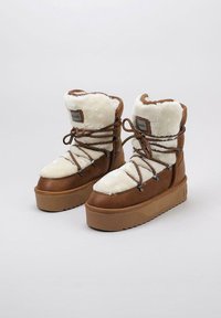 Botas de tobillo de cuero marrón con forro de lana blanca, que presentan una punta redonda, diseño con cordones y suela de goma gruesa y texturada.