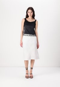 Črni satenski top brez rokavov z čipkastim robom na izrezu in ob robu, v kombinaciji z belim denimsko krilom. Črne sandale na vezalke dopolnjujejo videz.