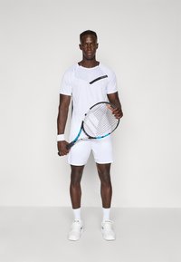 White tennis outfit with a short-sleeve shirt featuring a black accent, paired with white shorts. The player holds a tennis racket.