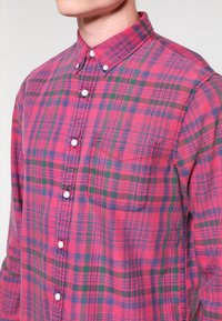 Czerwono-zielona koszula w kratę zapinana na guziki z lekkiego materiału, z kieszenią na lewej piersi i standardowym kołnierzykiem z białymi guzikami.