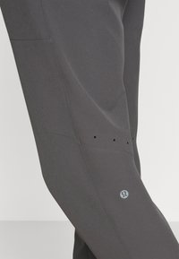 Szare spodenki sportowe wykonane z gładkiego materiału. Charakteryzują się subtelnym logo, bocznymi kieszeniami oraz małymi otworami wentylacyjnymi wzdłuż szwu.