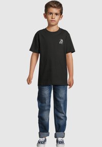 Black cotton t-shirt with a butterfly graphic on the chest, paired with blue denim jeans, featuring rolled cuffs and casual sneakers.
