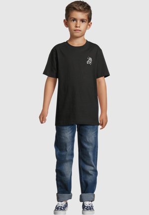 Camiseta negra de algodón con un gráfico de mariposa en el pecho, combinada con jeans de mezclilla azul, con puños enrollados y zapatillas informales.