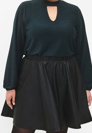 Mujer con un top de manga larga verde oscuro con escote en forma de ojo de cerradura y una falda negra en línea A con cinturilla elástica.