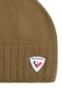 Gorro de punto marrón con textura acanalada, que presenta un parche de logo en colores rojo, blanco y azul en la esquina inferior derecha.