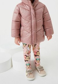 Rosa pufferjakke med en blank finish, parret med rosa leggings med Minnie Mouse-prints. Glitrende sneakers fuldender outfittet.