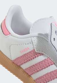 Biały sneaker z różowymi akcentami, fakturowanymi różowymi paskami i beżową gumową podeszwą. Posiada gładką skórzaną cholewkę i materiałowy język.