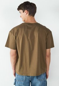 Brown cotton t-shirt with a crew neck, short sleeves, and a relaxed fit, featuring a smooth texture and simple design.