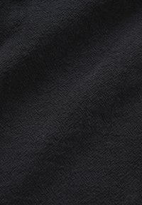 Gros plan sur la texture d'un tissu noir avec un motif subtil en diagonale et de doux plis créant des contrastes de lumière et d'ombre.