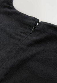 Garment in tessuto nero con chiusura a zip discreta in corrispondenza del collo, caratterizzato da una superficie liscia e dettagli delle cuciture minimi.