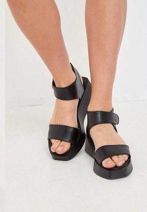 Sorte platformsandaler med brede, glatte remme og en struktureret sål. Har justerbar ankelrem og åben tå-design.