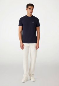 Donkerblauw katoenen T-shirt met een ronde hals, korte mouwen, subtiel logo op de borst, gecombineerd met witte broek en sneakers.