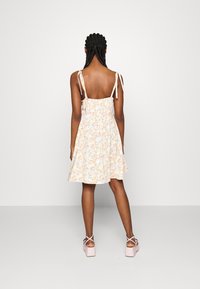 Robe d'été fleurie avec un dos froncé, des bretelles ajustables à nouer et une jupe évasée en jaune pastel et bleu, assortie à des chaussures à plateforme rose clair.