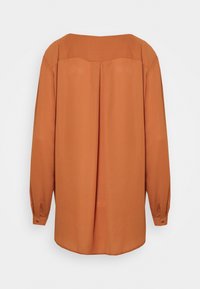 Halenka spáleně oranžové barvy s volným střihem, dlouhými rukávy a zapínáním na knoflíky na manžetách. Má zaoblený výstřih a střední zadní šev pro zvýraznění detailu.