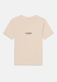 T-shirt à manches courtes beige clair en coton doux avec un col rond. Présente un petit imprimé noir "JJ Studios" sur la poitrine.