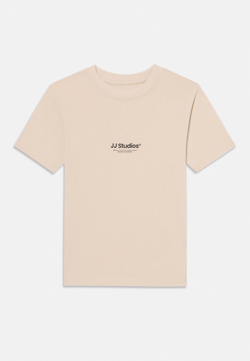 T-shirt à manches courtes beige clair en coton doux avec un col rond. Présente un petit imprimé noir "JJ Studios" sur la poitrine.