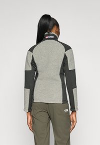 Chaqueta de forro polar con paneles grises y negros, cuello alto y un acabado texturizado. Presenta un logo en el cuello y un diseño ajustado.
