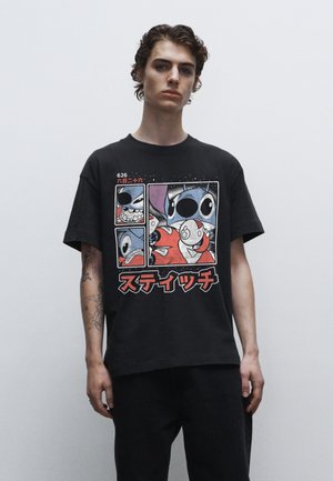 Sort bomulds t-shirt med et grafisk print af tegneseriefigurer i paneler, fremhævet med rød og hvid tekst, sat mod en ensfarvet baggrund.