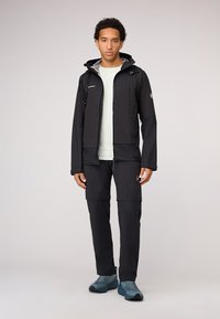 Chaqueta negra impermeable con capucha y cierre frontal, combinada con pantalones negros y zapatos en tono teal, con una textura suave y un diseño funcional.