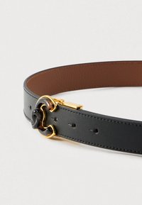 Juodas odinis diržas su ruda vidine pamušalu, pagamintas su auksinio tono sagtele ir vėžlio kiauto akcentu ant sagties.