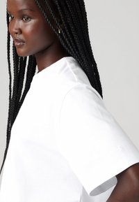 T-shirt blanc à manches courtes avec un col rond, fabriqué en tissu lisse, présentant un discret détail de logo près de l'ourlet.